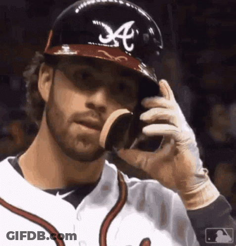 A Baseball Player Wearing A Helmet With The Letter A On It Is Eating A Cookie . GIF