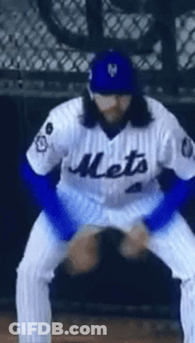 A Baseball Player Wearing A Mets Jersey And A Blue Hat Is Squatting Down On The Field . GIF