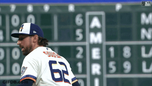 A Baseball Player Wearing A Number 62 Jersey Stands In Front Of A Scoreboard GIF