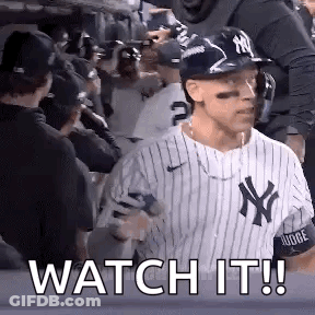 A Baseball Player Wearing A Ny Yankees Uniform Is Standing In Front Of A Crowd Of People . GIF