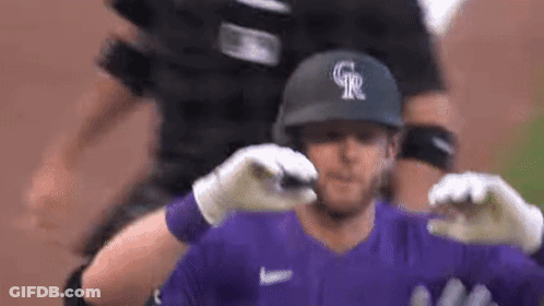 A Baseball Player Wearing A Purple Jersey And A Black Helmet Is Being Hugged By His Teammates . GIF