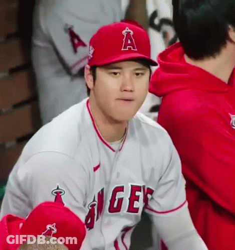 A Baseball Player Wearing A Red Hat And A White Jersey Is Sitting In A Dugout . GIF