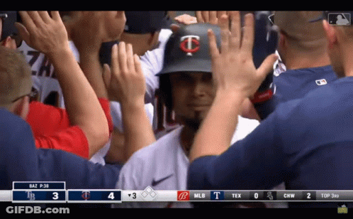 A Baseball Player With The Letter T On His Helmet Is Being High Fived By His Teammates GIF