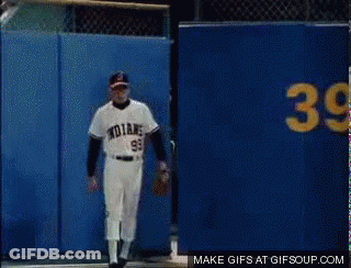 A Baseball Player With The Number 99 On His Jersey Stands In Front Of A Blue Wall GIF