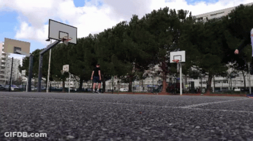 A Basketball Court With A Basketball Hoop And A Few Trees GIF