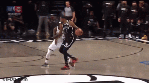 A Basketball Player Dribbles A Ball While Another Player Tries To Block Him GIF