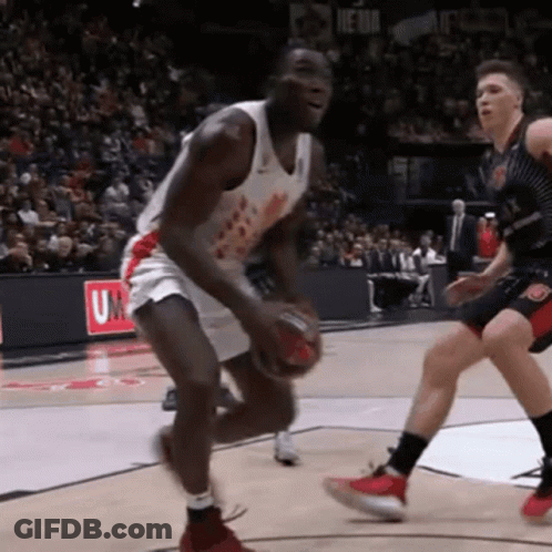 A Basketball Player Dribbles The Ball In Front Of A Sign That Says U On It GIF