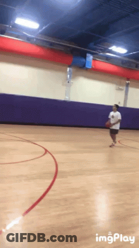 A Basketball Player Dribbles The Ball On A Court With A Purple Wall Behind Him GIF