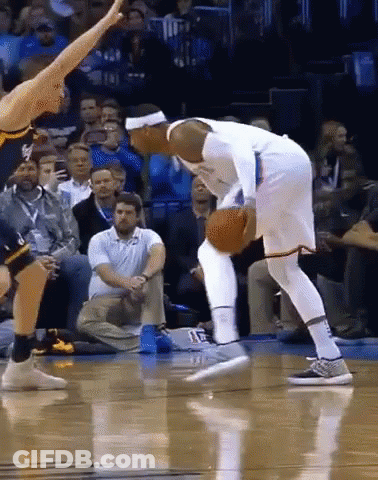 A Basketball Player Dribbles The Ball While Another Player Tries To Stop Him GIF