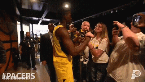 A Basketball Player Holds A Baby In His Arms In A Hallway With #Pacers On The Bottom GIF