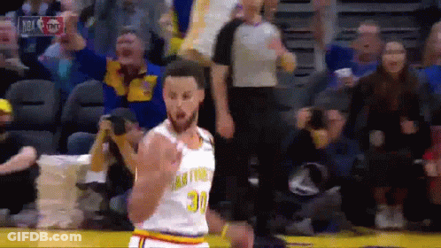 A Basketball Player In A Golden State Warriors Uniform Is Standing On The Court In Front Of A Crowd . GIF