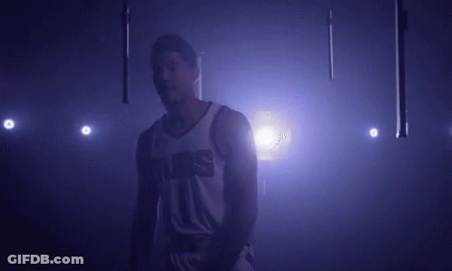 A Basketball Player In A Suns Jersey Is Standing In A Dark Room . GIF