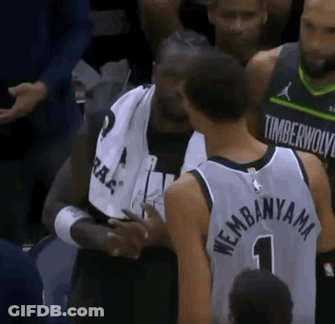 A Basketball Player In A Timberwolves Jersey Is Talking To Another Player In A Crowd . GIF