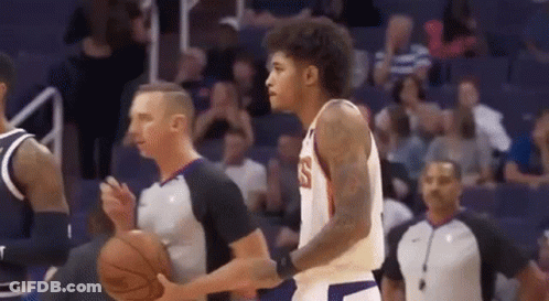 A Basketball Player Is Dribbling A Basketball While A Referee Looks On . GIF