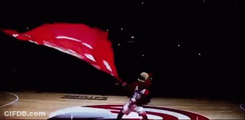 A Basketball Player Is Holding A Basketball In Front Of A Large Hawks Flag GIF