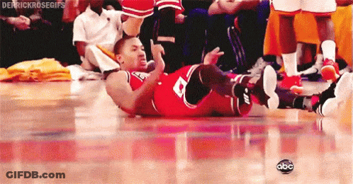 A Basketball Player Is Laying On His Back On The Floor While A Crowd Watches . GIF