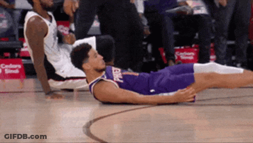 A Basketball Player Is Laying On The Floor While Another Player Sits On The Bench GIF