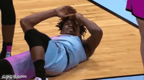 A Basketball Player Is Laying On The Floor With His Head On His Knees . GIF