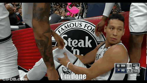 A Basketball Player Is Laying On The Ground With A Steak 'N ' Sign In The Background GIF