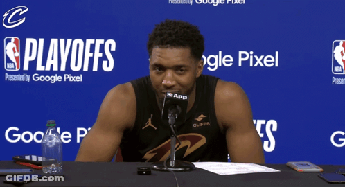 A Basketball Player Is Sitting At A Table With A Microphone In Front Of A Blue Background That Says Playoffs GIF