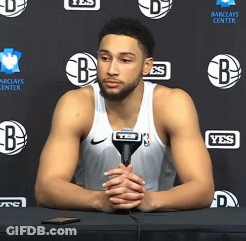 A Basketball Player Is Sitting At A Table With A Microphone In Front Of A Wall That Says Yes GIF