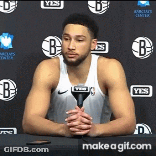 A Basketball Player Is Sitting At A Table With A Microphone In Front Of Him . GIF