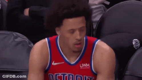 A Basketball Player Is Sitting In The Stands During A Game Wearing A Red Jersey With The Word Detroit On It . GIF