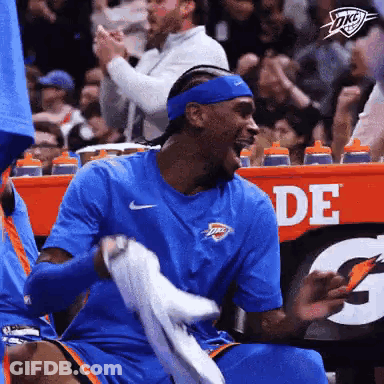A Basketball Player Is Sitting In The Stands Holding A Towel And Laughing . GIF