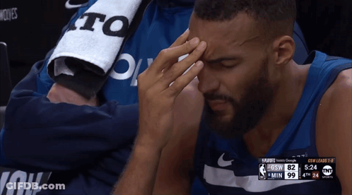 A Basketball Player Is Sitting In The Stands With His Hand On His Forehead During A Game GIF