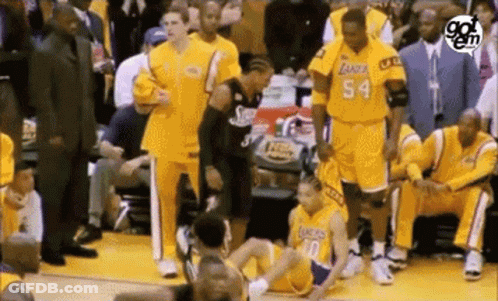A Basketball Player Is Sitting On The Floor During A Game While A Group Of Basketball Players Are Standing Around Him . GIF