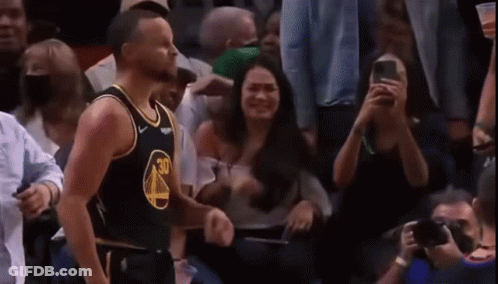 A Basketball Player Is Standing In Front Of A Crowd Of People While A Woman Takes A Picture Of Him . GIF