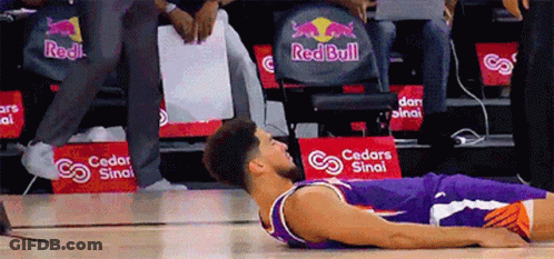 A Basketball Player Laying On The Floor In Front Of A Red Bull Ad GIF