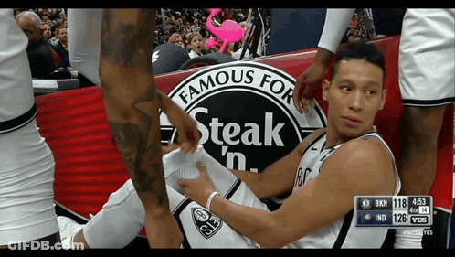 A Basketball Player Laying On The Floor With A Steak 'N Advertisement In The Background GIF