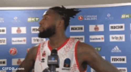 A Basketball Player Stands In Front Of A Blue Wall With Turkish Airlines And Fedecom Logos On It GIF