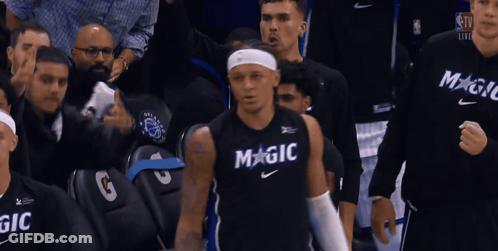 A Basketball Player Wearing A Black Magic Jersey Stands In Front Of A Crowd GIF