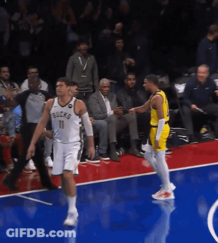 A Basketball Player Wearing A Bucks Jersey Talks To Another Player On The Court GIF