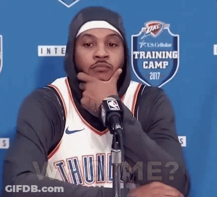 A Basketball Player Wearing A Hoodie Is Standing In Front Of A Microphone With His Hand On His Chin . GIF