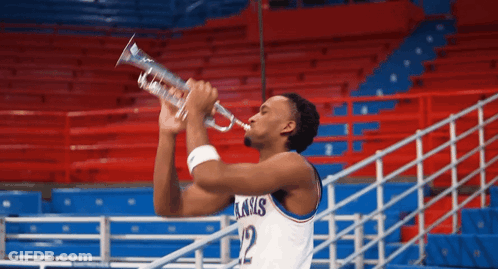 A Basketball Player Wearing A Kansas Jersey Is Blowing A Trumpet GIF
