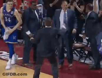 A Basketball Player Wearing A Kansas Jersey Is Walking On The Court With A Group Of Men . GIF
