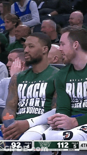 A Basketball Player Wearing A Shirt That Says Black Story Voices Sits In The Stands GIF