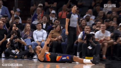 A Basketball Player Wearing A Suns Uniform Is Laying On The Floor GIF