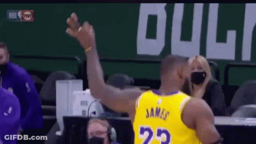 A Basketball Player Wearing A Yellow Jersey With The Number 23 On The Back Is Raising His Arm In The Air . GIF