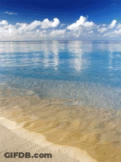 A Beach With A Blue Sky And Clouds Reflected In The Ocean GIF