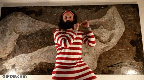 A Bearded Man In A Red And White Striped Shirt Stands In Front Of A Painting GIF