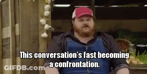 A Bearded Man Wearing Overalls And A Red Hat Is Sitting In Front Of Garlic . GIF