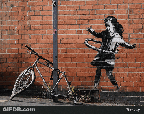 A Bicycle Is Parked In Front Of A Brick Wall With A Painting Of A Girl With A Hula Hoop GIF