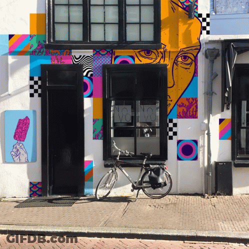 A Bicycle Is Parked In Front Of A Building With A Colorful Mural GIF