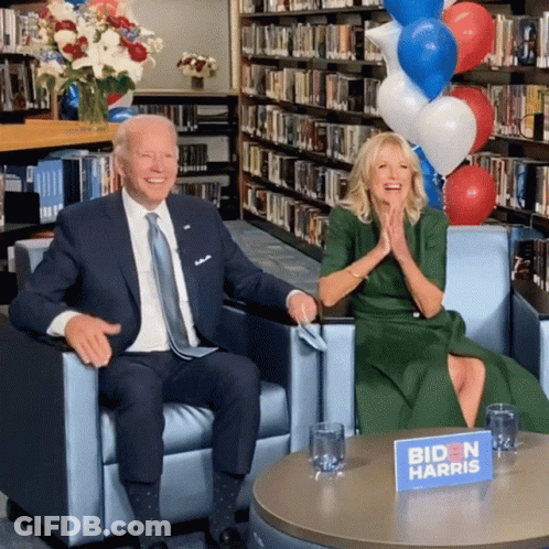 A Biden Harris Sign Sits On A Table Next To A Man In A Suit GIF