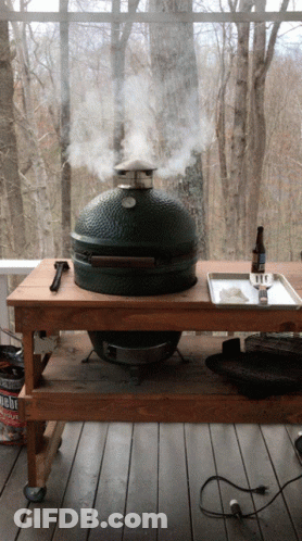 A Big Green Egg Grill Is Smoking A Piece Of Meat On A Wooden Table GIF