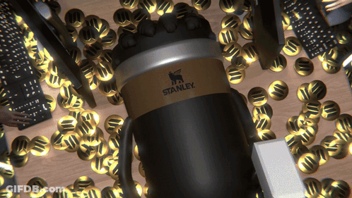 A Black And Gold Stanley Coffee Mug Is Surrounded By Gold Coins GIF